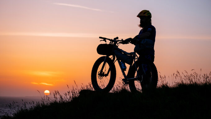 Man with a fatbike in front of a sunset