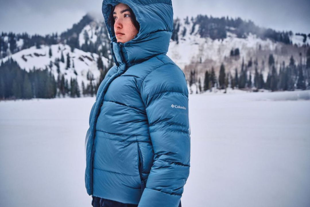 Une personne avec un manteau bleu Columbia devant une montagne enneigée