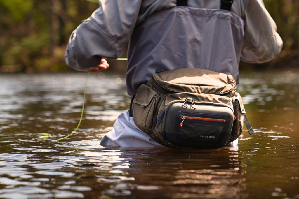 an angler seen from behind fishing in a stream, wearing fishing clothing and gear