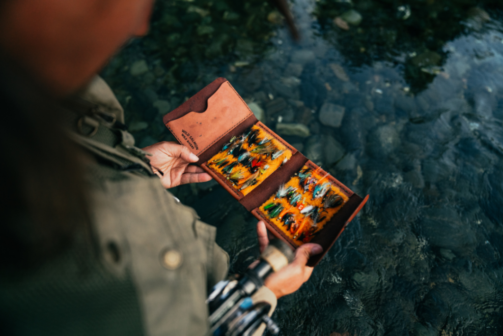 an angler wearing a fishing jacket and carrying a fly rod holds a Hooké fly wallet containing flies used for fly fishing for Atlantic salmon
