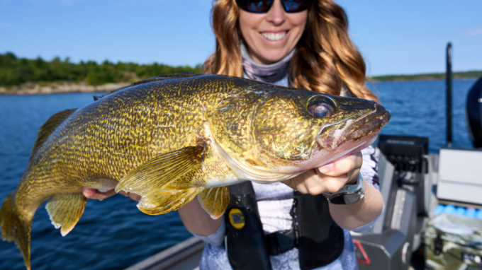 Ashley Rae holding a large walleye during a summer walleye fishing trip on a lake