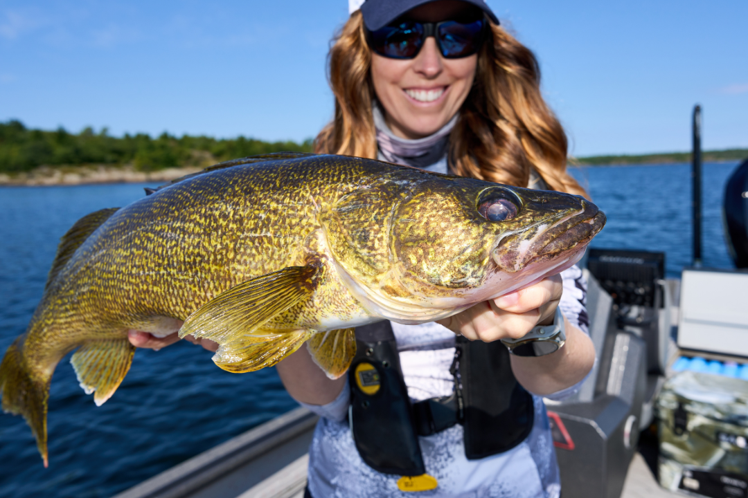 Ashley Rae holding a large walleye during a summer walleye fishing trip on a lake